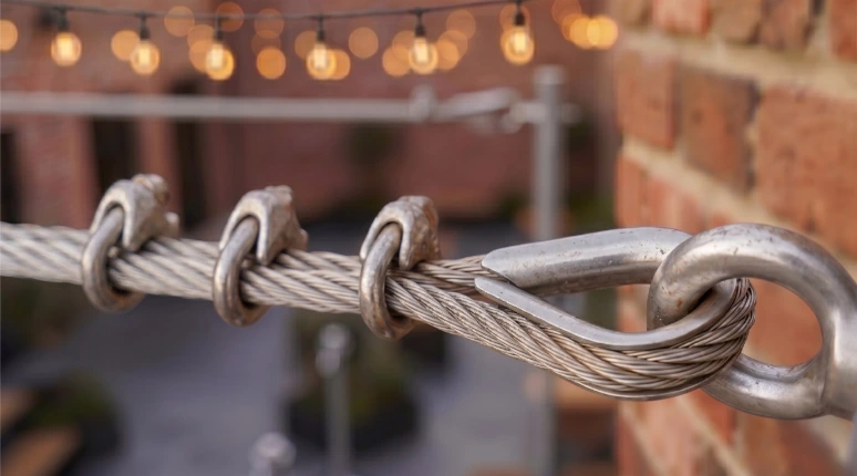 Stainless steel catenary wire rope kit with wire rope grips, thimble, and eye bolt anchor on brick wall