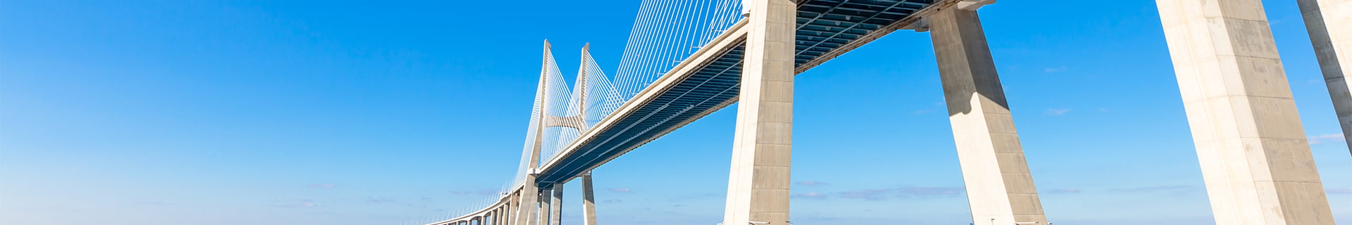 Modern white cable-stayed bridge with concrete support pillars against a clear blue sky.