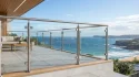Satin finish stainless steel glass balustrading posts with round handrail on outdoor coastal balcony.